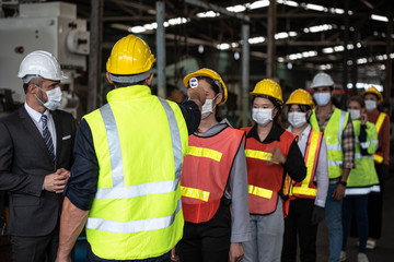 Factory manager and Staff checking fever digital thermometer for industrial workers before working inside factory to prevent Coronavirus inflection. They wear surgical mask and hardhat or helmet, vest