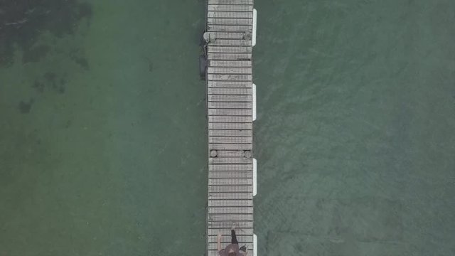 Overhead shot of couple walking on narrow wooden bridge by water in NZ