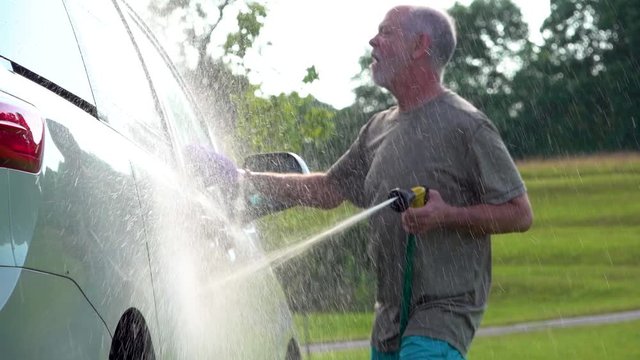 Slow motion of man washing his car and dancing with the hose and soapy rag.