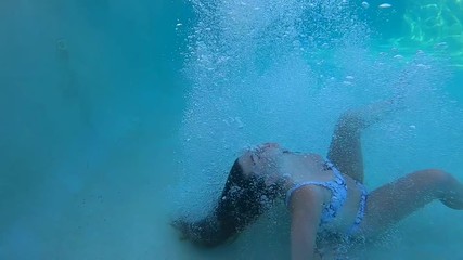 Young Caucasian teenage girl wearing bikini bathing suit jumps and does cannonball into clear fresh blue water outdoor pool on sunny summer day, handheld close up profile