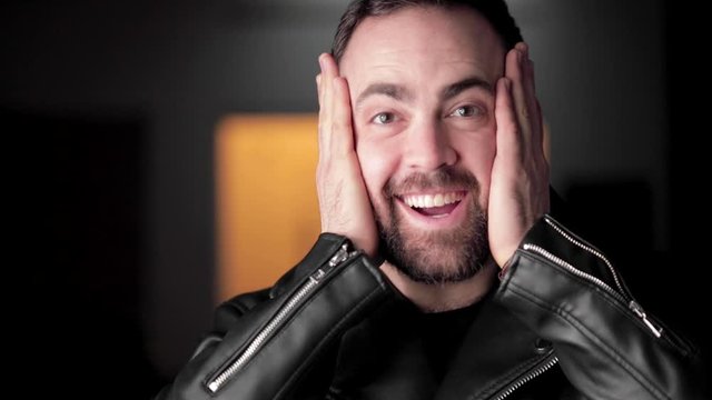 Handsome bearded man in jacket gesticulates and laughs into camera, close up