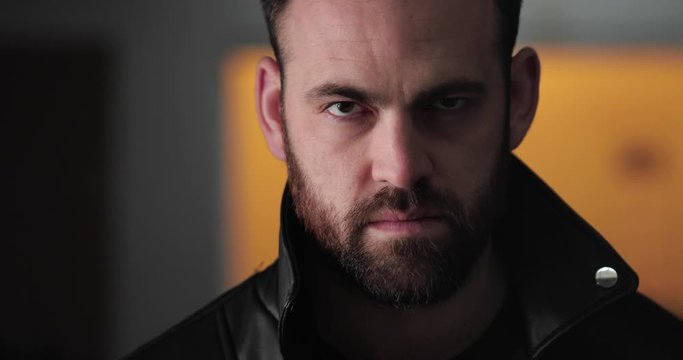 Dark, mean looking man steps out of shadows and glares into camera, close up