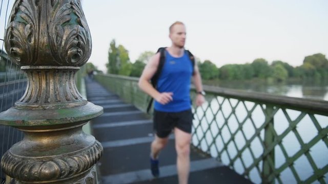 A man jogging into focus across a bridge