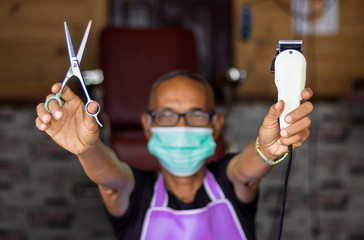 Both hands of the male barber held the clippers and scissors.