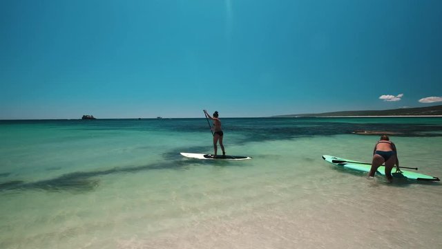 Slow motion shot of two women in bikini using Stand Up Paddle Board for Paddleboarding in Australia