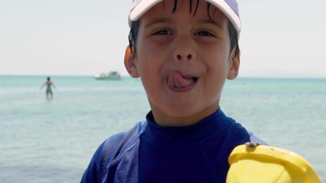 Close up on face of caucasian kid smiling at camera, with sea in the blurry background, slow motion 120fps