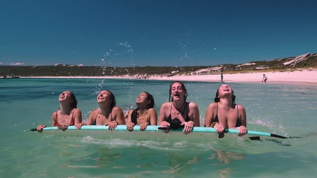 Panning shot of sexy bikini models lying on board in beautiful ocean and throwing hairs in slow motion