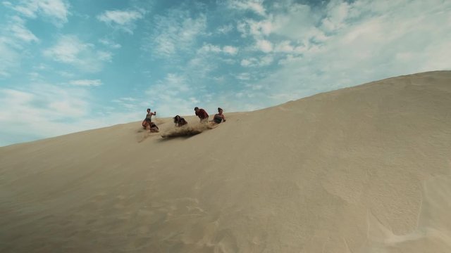 Shot of people jumping and rolling down from a sand dune.