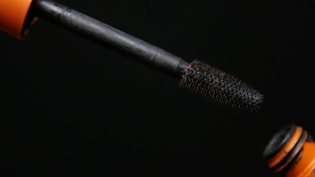 Woman's hand opens up mascara tube to reveal the brush with product on it.
