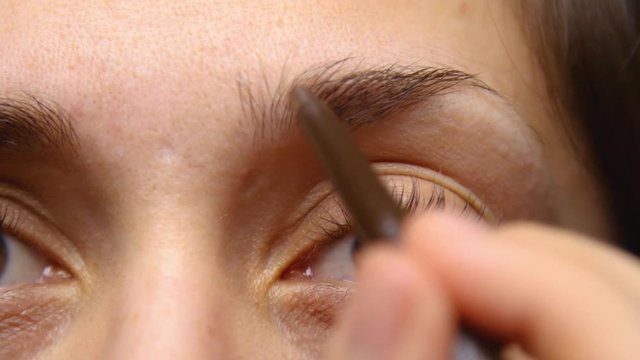 Woman fills in her eyebrows with a brow pencil.