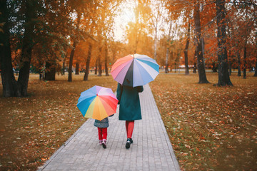 a small child with mother in a warm suit and with a colorful umbrella walks in the woods. autumn park. The concept of children's fashion, accessories, outdoor walks