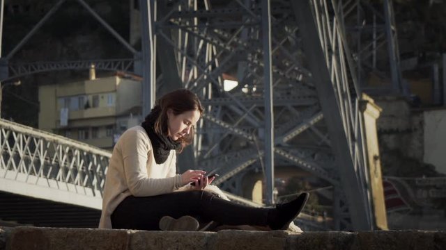 Gorgeous Lady Using Smartphone While Sitting By The Steel Bridge Structure In Porto, Portugal - full slowmo shot
