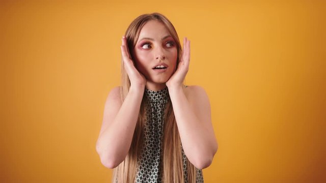 Girl is covering the sides of her face with her hands and looking confused around. Isolated on yellow