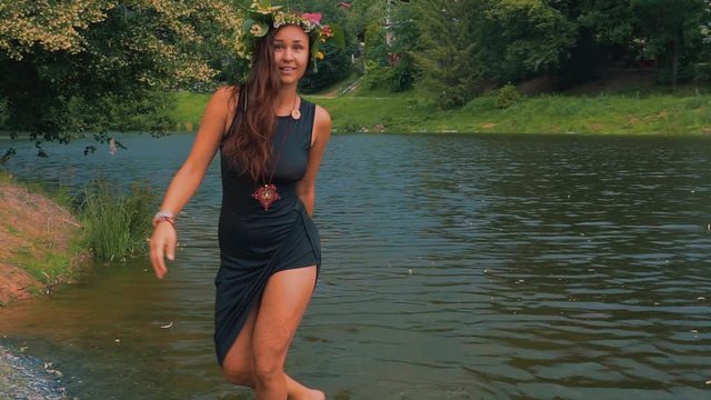 Attractive Young Woman With Flower Wreath on Head Standing in Lake, Slow Motion, Playing With Water. Freedom and Folk Spirituality Concept