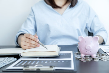 The young woman checks to account a piggy bank and dollar note on the table, step up start-up business to success, Saving money for future plan and retirement fund concept