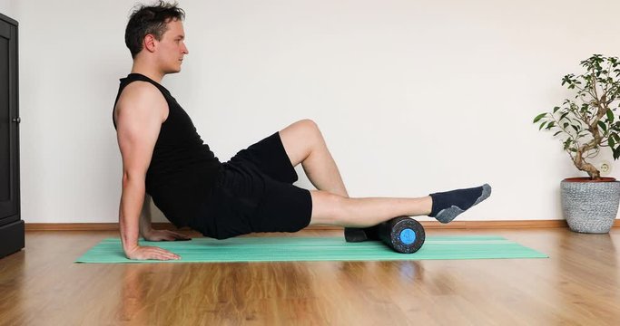 young man doing his workout at home in the living room with black roll for fascia training