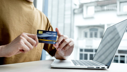 Businessman hand hold credit card to online shopping on laptop computer from home, payment e-commerce, internet banking, spending money