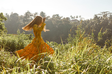 Summertime and lifestyle. Young unrecognizable carefree woman enjoying dancing freedom and sunny nature scene. Picturesque view of countryside at background..