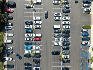 Aerial top view of parking lot at shopping mall with varieties of colored vehicles. People walking to their car and trying to park.