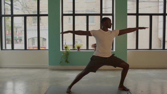 African American black male athletic leans into standing yoga warrior pose as camera pulls back, and pushes back in wide to medium. 4K, gimbal.