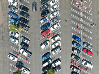 Aerial top view of parking lot at shopping mall with varieties of colored vehicles. People walking to their car and trying to park.