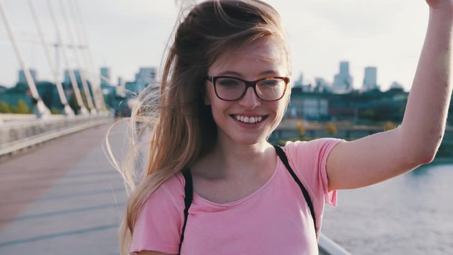 Portrait of young happy woman adjusting her hair on the wind while standing on the bridge. Slow motion
