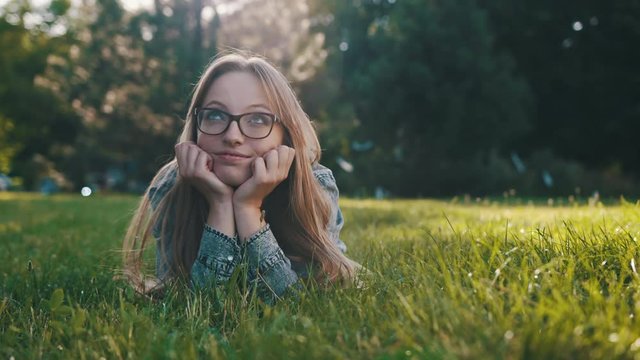 Young caucasian brunette with glasses lying on the grass in the park and thinking. Relaxation in the nature