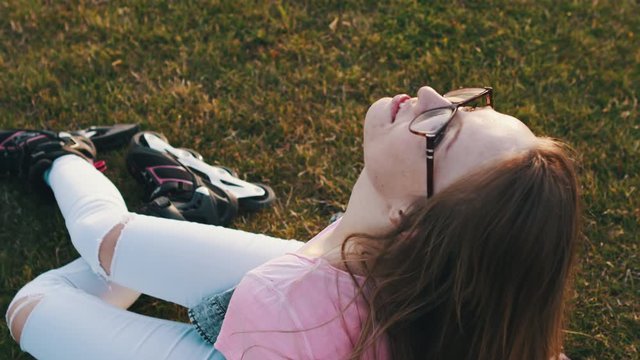 A teenage girl with roller blades on her feet relaxing on the meadow. Freedom and daydreaming concept