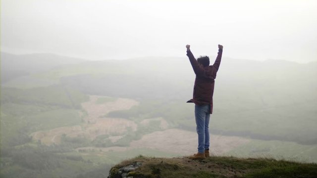 Man Raising Arms Victoriously After Climbing to the top of Mountain on Windy Day