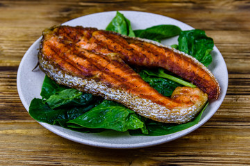 Plate with roasted salmon steak and spinach leaves on a wooden table