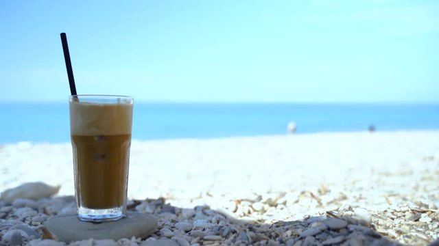 Frapp&eacute; Greek coffee iced drink on pebbles beach with blue sea and sky background, vacation concept