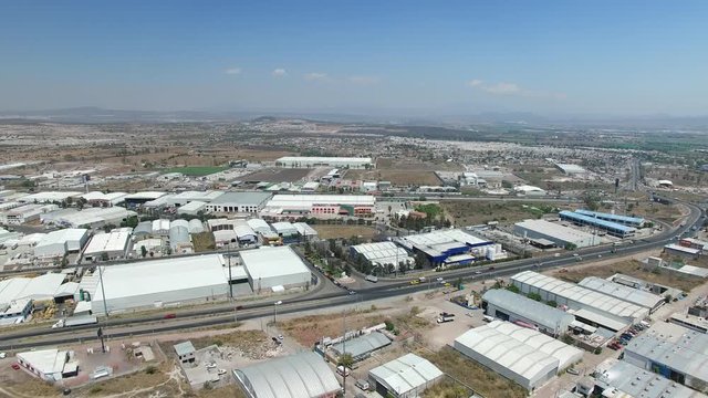 Vista a&eacute;rea panor&aacute;mica de la zona industrial de Quer&eacute;taro. El drone volando hacia atr&aacute;s con un cielo azul como fondo y cruzando la autopista