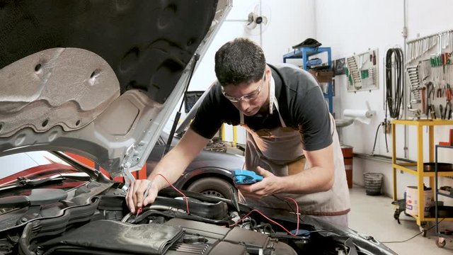 Mechanic checking a car with a multimeter in garage with tools on the wall