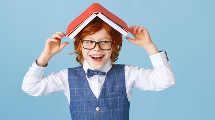 Happy schoolboy playing with book.
