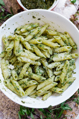 A bowl of Pesto Sauce and Penne Rigatoni Pasta with a small bowl of dark pesto sauce in the background. The bowl of pasta is topped with white Parmesan cheese. 