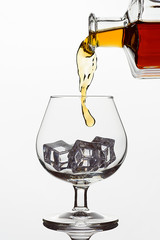 Fototapeta na wymiar Clear glass glass with ice cubes. Frozen stream from a bottle of whiskey or cognac or brandy on a white isolated background