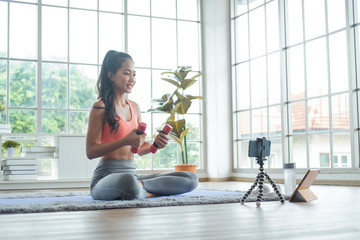 Young asian woman exercise with dumbbell while online tutorial on mobile phone.