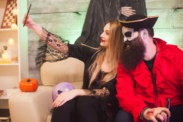 Vampire woman taking a selfie with smiling pirate at halloween celebration.