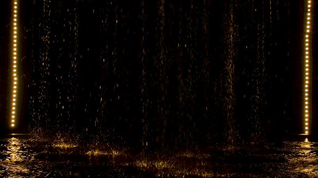 Yellow spatters rain fall against the background of a stage lighting in dark studio. Slow motion.