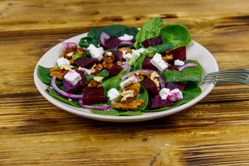 Tasty spinach salad with boiled beetroot, feta cheese, walnut and red onion on wooden table. Healthy vegetarian food