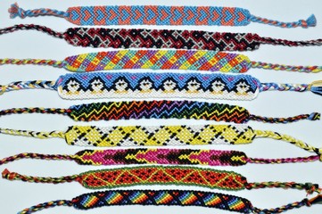 Multi-colored woven friendship bracelets handmade of embroidery bright thread with knots on light gray background