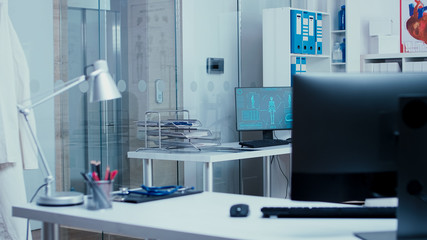 Modern private clinic interior with hallway and elevator. Computer in desk displaying a high tech technology futuristic MRI X Ray scan. Treatment equipment and professional tools. Consultation room