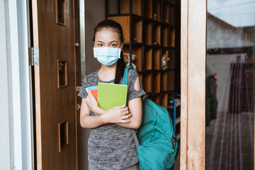 Fototapeta na wymiar an Asian teenage girl standing wearing a mask and backpack carrying a book before going out to return to school after a pandemic