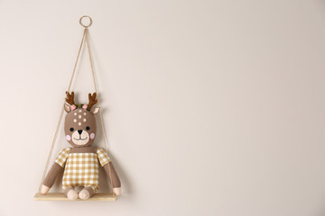 Shelf with cute toy deer on beige wall, space for text. Child's room interior element