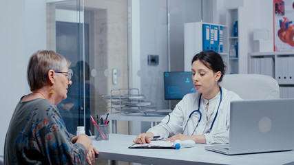 Doctor doing a temperature check in office to senior retired woman patient. Healthcare in modern hospital or private clinic, disease prevention and consultation in medic office treatment medication