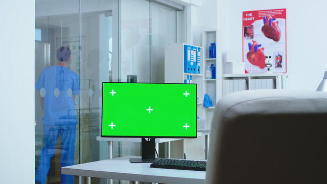 Computer with copy space available in hospital and assistant going in elevator. Desktop with blank green screen mockup isolated space available on of medicine specialist in clinic cabinet.