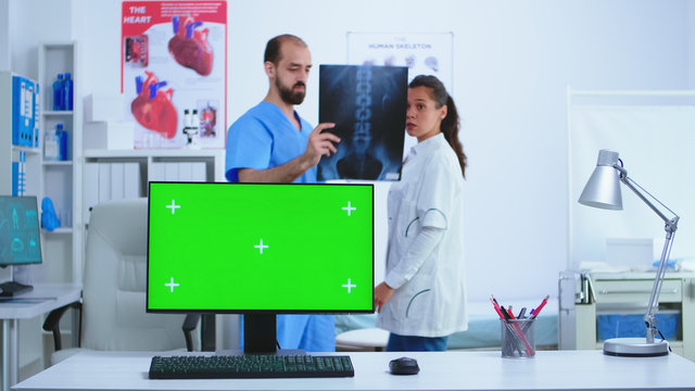 Monitor in hospital cabinet with chroma key while doctor and nurse checking x-ray image. Desktop with replaceable screen in medical clinic while doctor is checking patient radiography for diagnose.