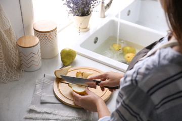 Woman cutting fresh ripe pear at table in kitchen, closeup