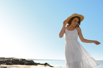 Fototapeta na wymiar Happy young woman with hat on beach near sea. Space for text