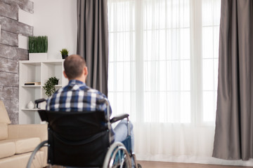 Lonely man in wheelchair with walking disability in living room. Serious sad caucasian man wearing...